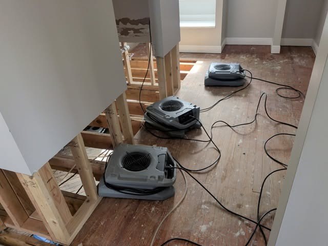 Air movers drying a room after wet drywall was removed